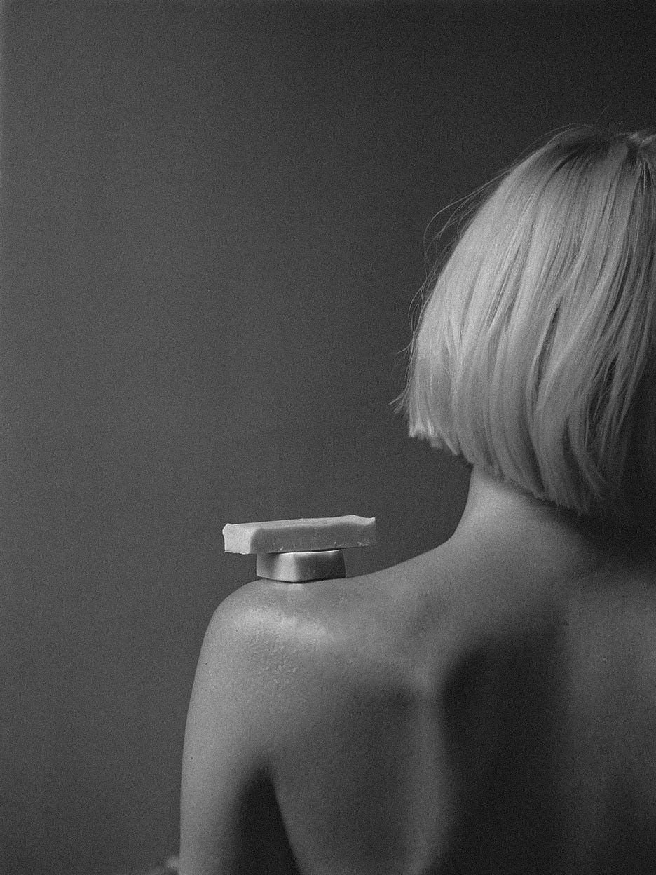 Black and white photograph of a person with a bar of soap on their shoulder against a dark background